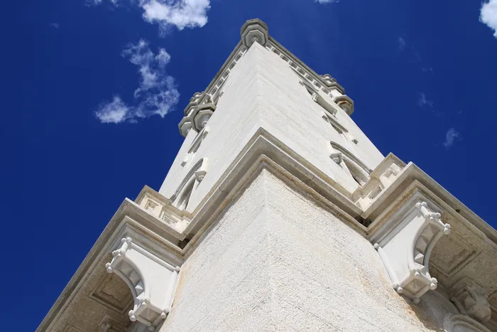 La torre del castello vista dal basso contro il cielo azzurro, con i merli e i beccatelli in pietra bianca